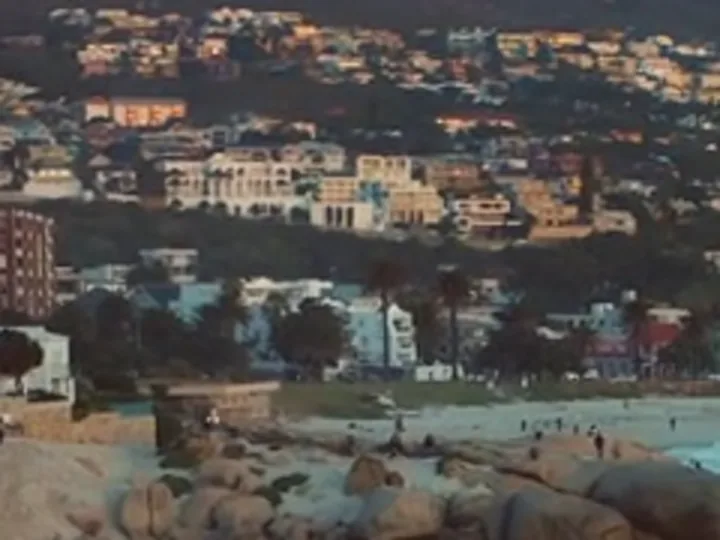 Crop of a 1280×720 drone frame at sunset, houses on a hillside above a beach, enlarged with bicubic scaling