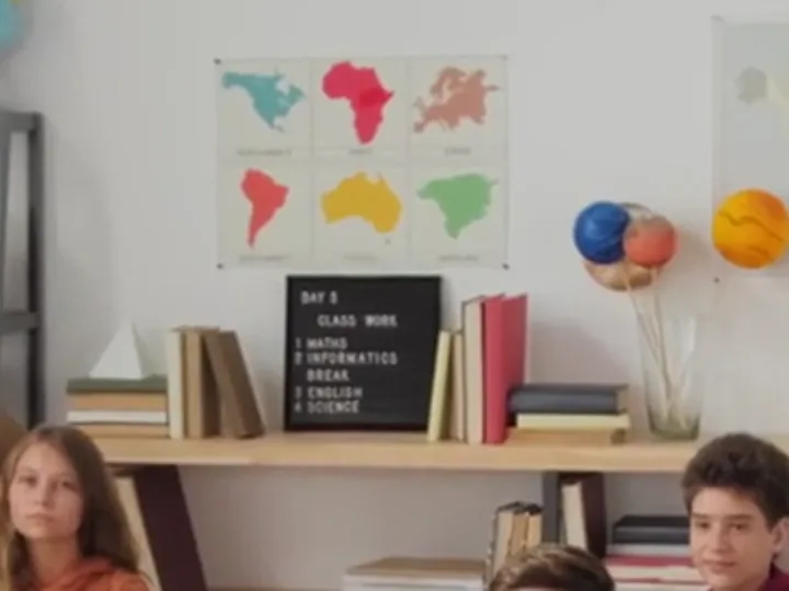 Crop of a 1280×720 classroom frame with a letter board and wall maps, enlarged with bicubic scaling